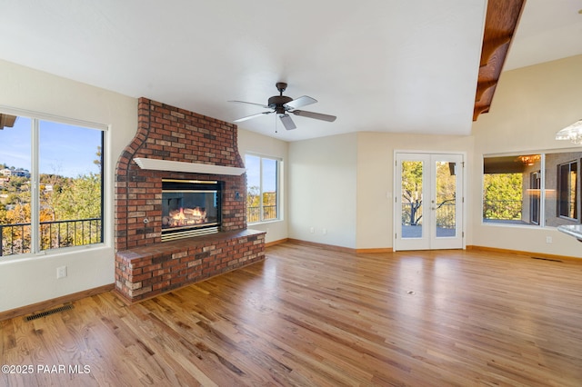 unfurnished living room with a fireplace, light hardwood / wood-style floors, french doors, and ceiling fan