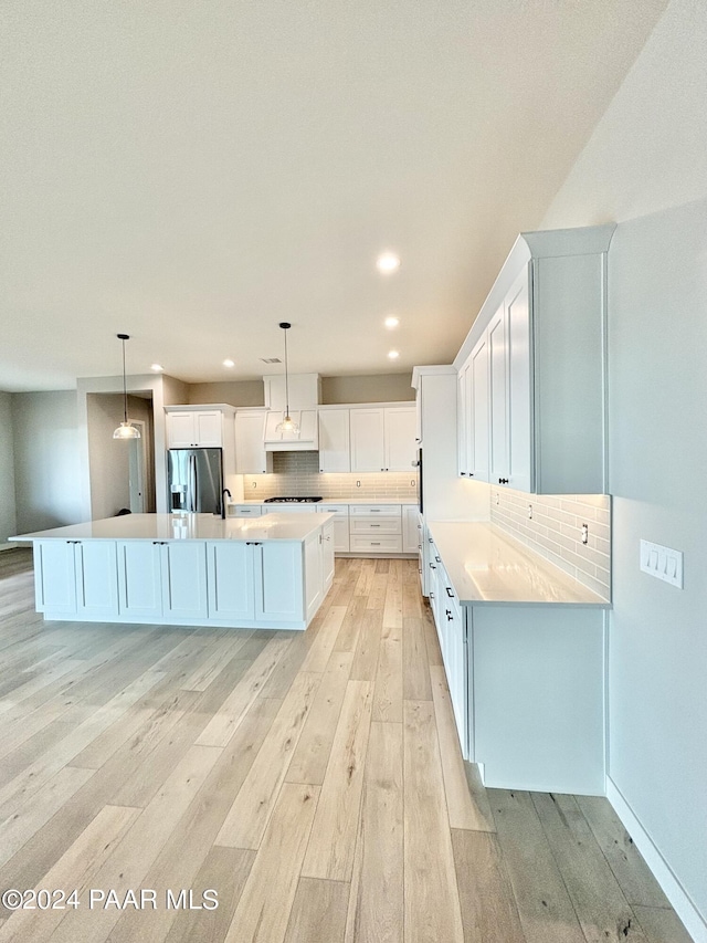 kitchen featuring pendant lighting, stainless steel refrigerator with ice dispenser, light hardwood / wood-style flooring, a large island, and white cabinetry