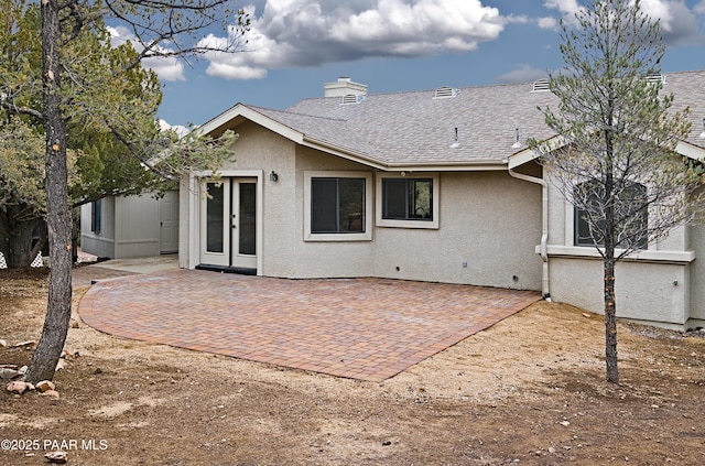 back of house featuring roof with shingles, stucco siding, french doors, a chimney, and a patio