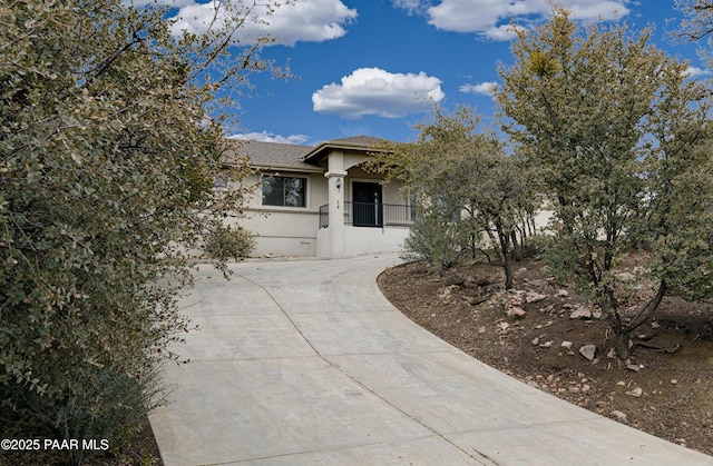 view of front of house featuring roof with shingles, driveway, and stucco siding