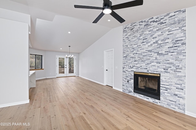 unfurnished living room featuring vaulted ceiling, a stone fireplace, ceiling fan with notable chandelier, and wood finished floors