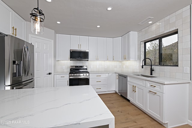 kitchen featuring visible vents, a sink, appliances with stainless steel finishes, light wood finished floors, and decorative backsplash