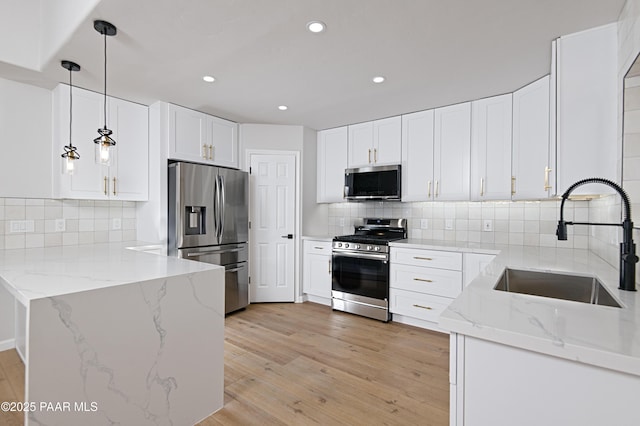 kitchen featuring a sink, stainless steel appliances, light wood-style floors, a peninsula, and light stone countertops