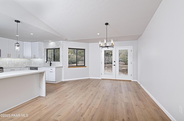 kitchen with backsplash, light countertops, an inviting chandelier, white cabinetry, and a sink