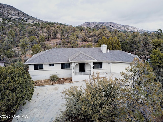 single story home featuring a forest view, a mountain view, an attached garage, a shingled roof, and a chimney