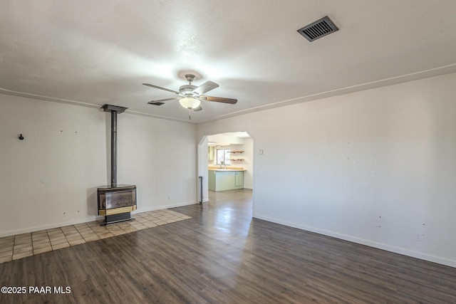 unfurnished living room featuring arched walkways, wood finished floors, visible vents, a ceiling fan, and a wood stove