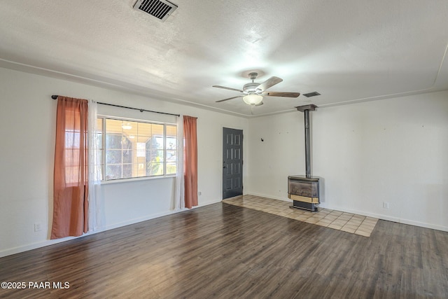 unfurnished living room featuring visible vents, a ceiling fan, a wood stove, a textured ceiling, and wood finished floors