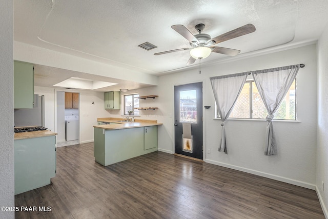 kitchen featuring washer / clothes dryer, a peninsula, light countertops, green cabinets, and a sink