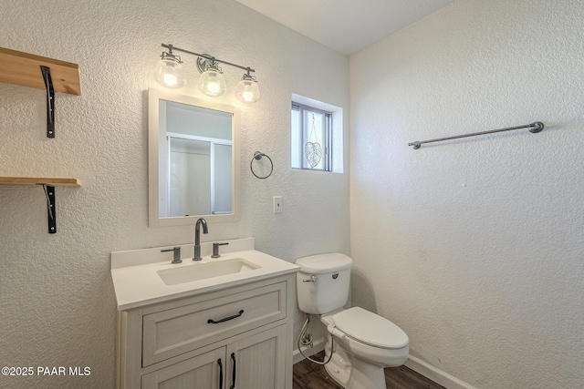 full bathroom featuring a textured wall, toilet, vanity, wood finished floors, and baseboards