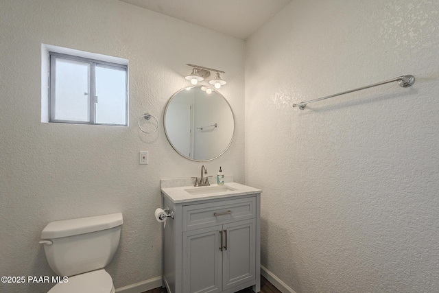 bathroom with a textured wall, vanity, and toilet