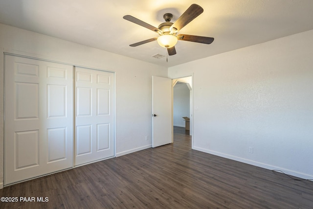 unfurnished bedroom featuring dark wood-style floors, arched walkways, a closet, visible vents, and baseboards