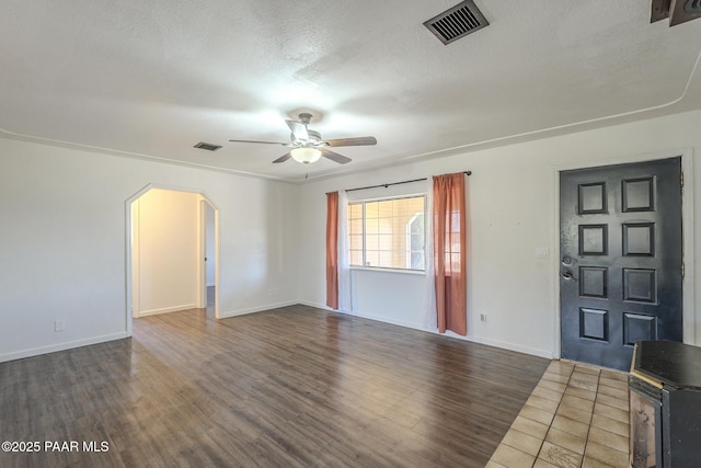 unfurnished living room with dark wood-style floors, arched walkways, visible vents, and a ceiling fan