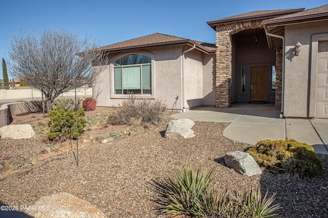 property entrance featuring stone siding, roof with shingles, and stucco siding