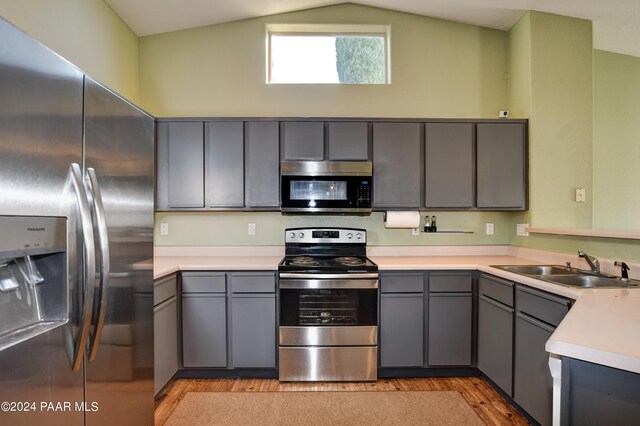 kitchen with appliances with stainless steel finishes, light hardwood / wood-style floors, lofted ceiling, and gray cabinetry