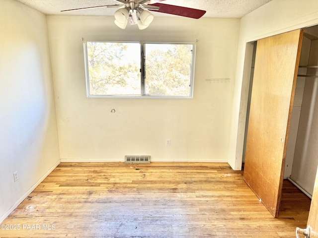 unfurnished bedroom featuring ceiling fan, a closet, a textured ceiling, and light wood-type flooring