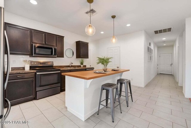 10429 W Crown King Rd, Tolleson, AZ 85353 - kitchen featuring appliances with stainless steel finishes, a sink, dark brown cabinets, butcher block counters, and a kitchen bar