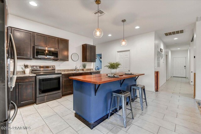 10429 W Crown King Rd, Tolleson, AZ 85353 - kitchen featuring appliances with stainless steel finishes, butcher block counters, dark brown cabinets, a kitchen breakfast bar, and pendant lighting
