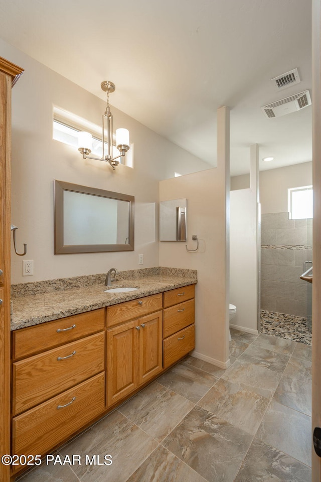 bathroom with a tile shower, an inviting chandelier, toilet, and vanity