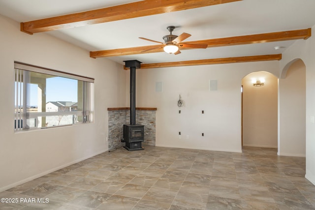 unfurnished living room featuring ceiling fan, a wood stove, and beamed ceiling