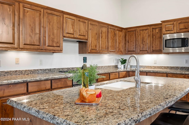 kitchen with light stone countertops, stainless steel microwave, a breakfast bar area, and sink