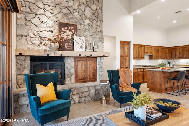 living room with a stone fireplace, a towering ceiling, and sink