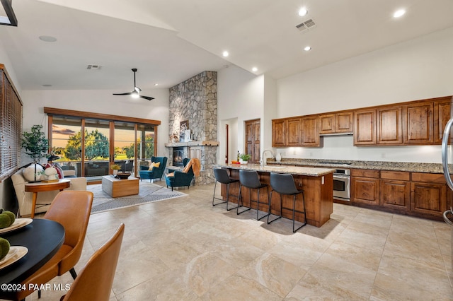 kitchen featuring light stone countertops, ceiling fan, stainless steel appliances, a kitchen island with sink, and a breakfast bar