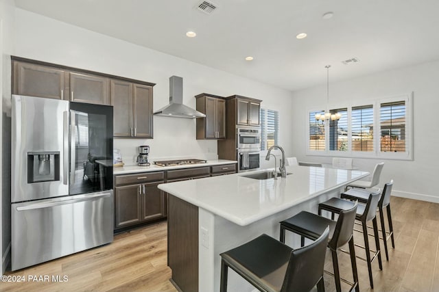 kitchen with sink, a breakfast bar area, appliances with stainless steel finishes, decorative light fixtures, and wall chimney exhaust hood