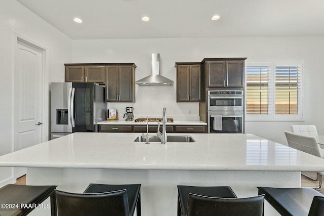 kitchen featuring a kitchen island with sink, wall chimney range hood, stainless steel appliances, and sink