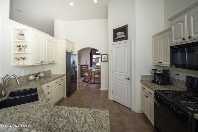 kitchen featuring light stone countertops, sink, black appliances, and a high ceiling