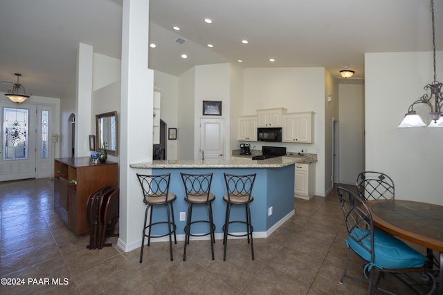 kitchen with light stone countertops, kitchen peninsula, pendant lighting, white cabinets, and black appliances