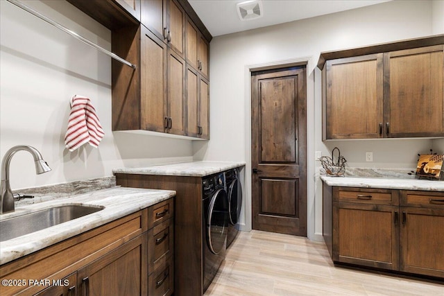 washroom with visible vents, washing machine and dryer, cabinet space, a sink, and light wood-style floors