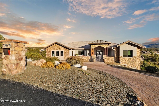 mediterranean / spanish-style house with curved driveway, stucco siding, and stone siding