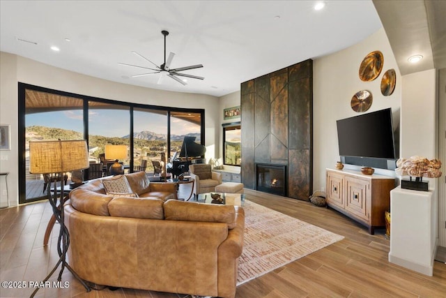 living area featuring light wood finished floors, ceiling fan, a wealth of natural light, and a fireplace