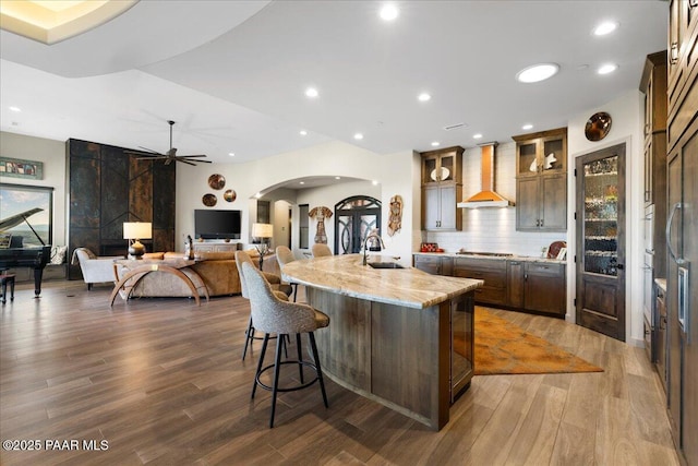 kitchen featuring a sink, stainless steel gas cooktop, ceiling fan, wall chimney range hood, and arched walkways