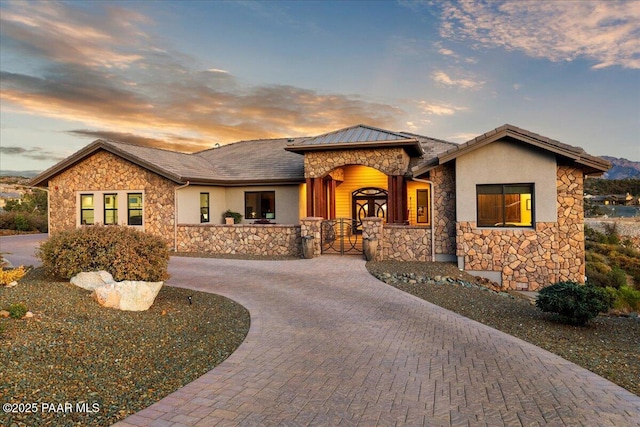 view of front facade featuring curved driveway, stucco siding, and stone siding