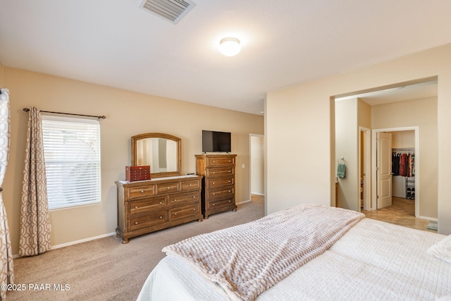 bedroom featuring light colored carpet, a walk in closet, visible vents, and baseboards