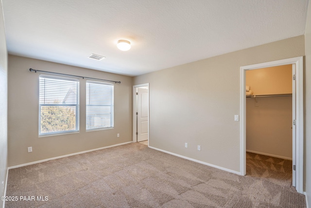 unfurnished bedroom with light colored carpet, visible vents, baseboards, a spacious closet, and a closet