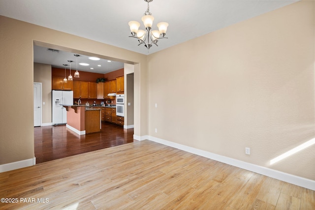 unfurnished living room featuring a notable chandelier, visible vents, baseboards, and wood finished floors