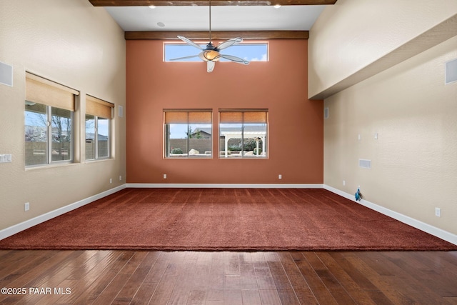 unfurnished living room featuring beam ceiling, a towering ceiling, baseboards, and wood finished floors