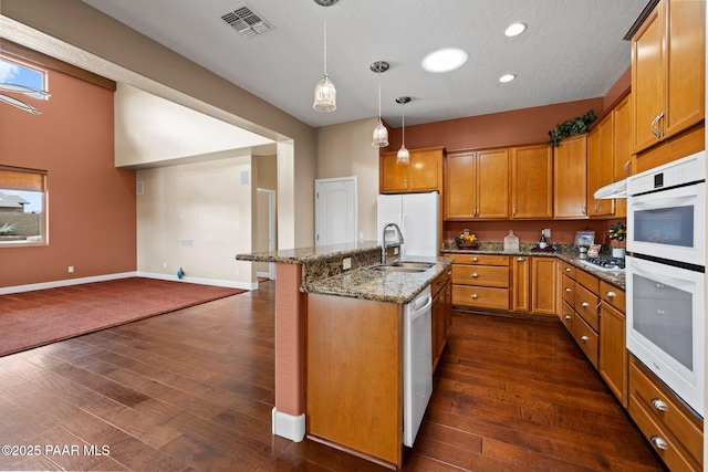 kitchen featuring white appliances, brown cabinetry, visible vents, an island with sink, and a sink