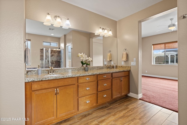 full bath with visible vents, a shower stall, double vanity, wood finished floors, and a sink