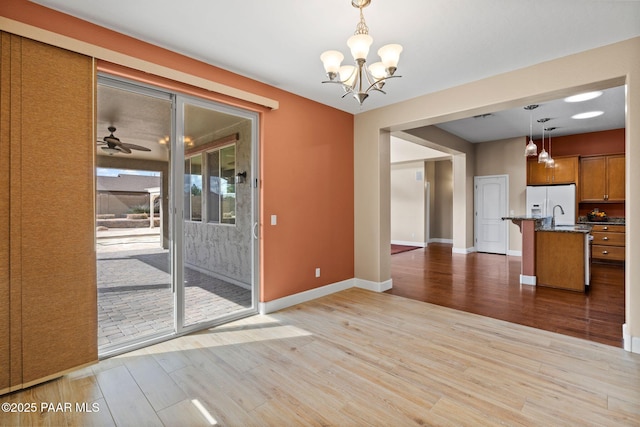 interior space featuring light wood-style flooring, ceiling fan with notable chandelier, baseboards, and a sink