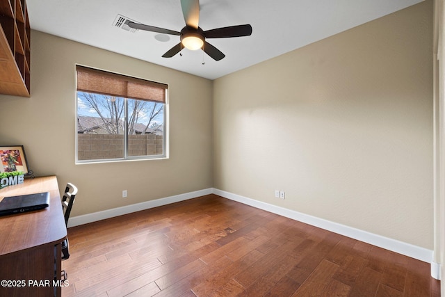 unfurnished office featuring dark wood-style floors, visible vents, a ceiling fan, and baseboards