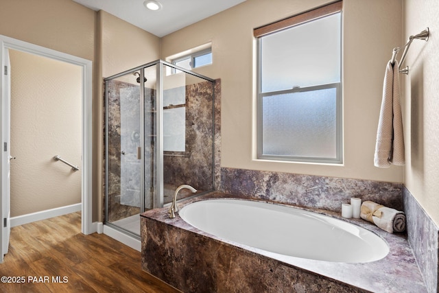 bathroom featuring a bath, a stall shower, baseboards, and wood finished floors