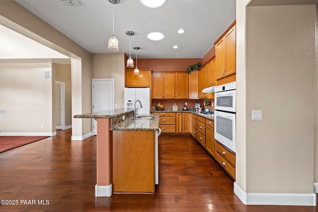 kitchen featuring white appliances, dark wood-style floors, baseboards, stone countertops, and a sink