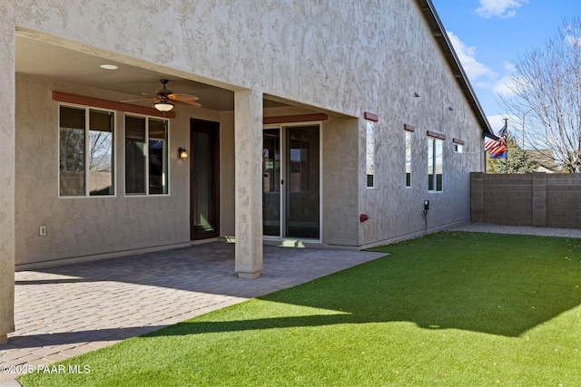 rear view of house with a patio area, stucco siding, a lawn, and a ceiling fan