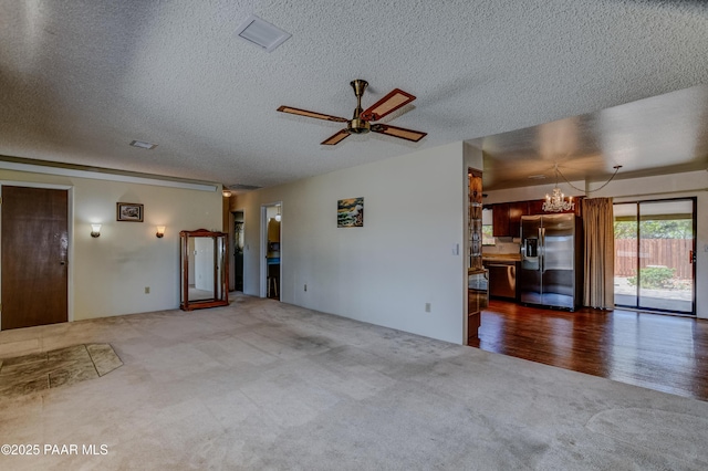 unfurnished living room with carpet floors, a textured ceiling, ceiling fan with notable chandelier, and visible vents