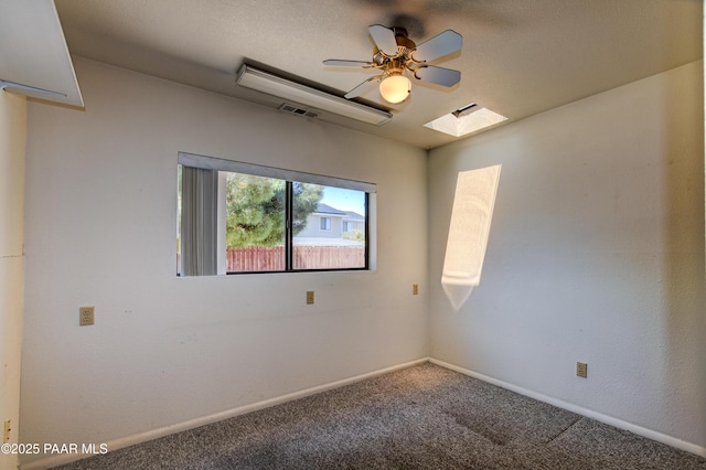 carpeted empty room featuring baseboards, ceiling fan, visible vents, and a skylight