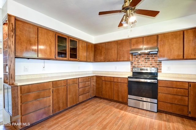 kitchen featuring under cabinet range hood, stainless steel electric stove, brown cabinetry, and light wood-style flooring