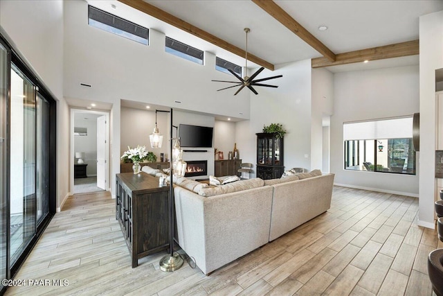 living room featuring beamed ceiling, a towering ceiling, light wood-type flooring, and ceiling fan